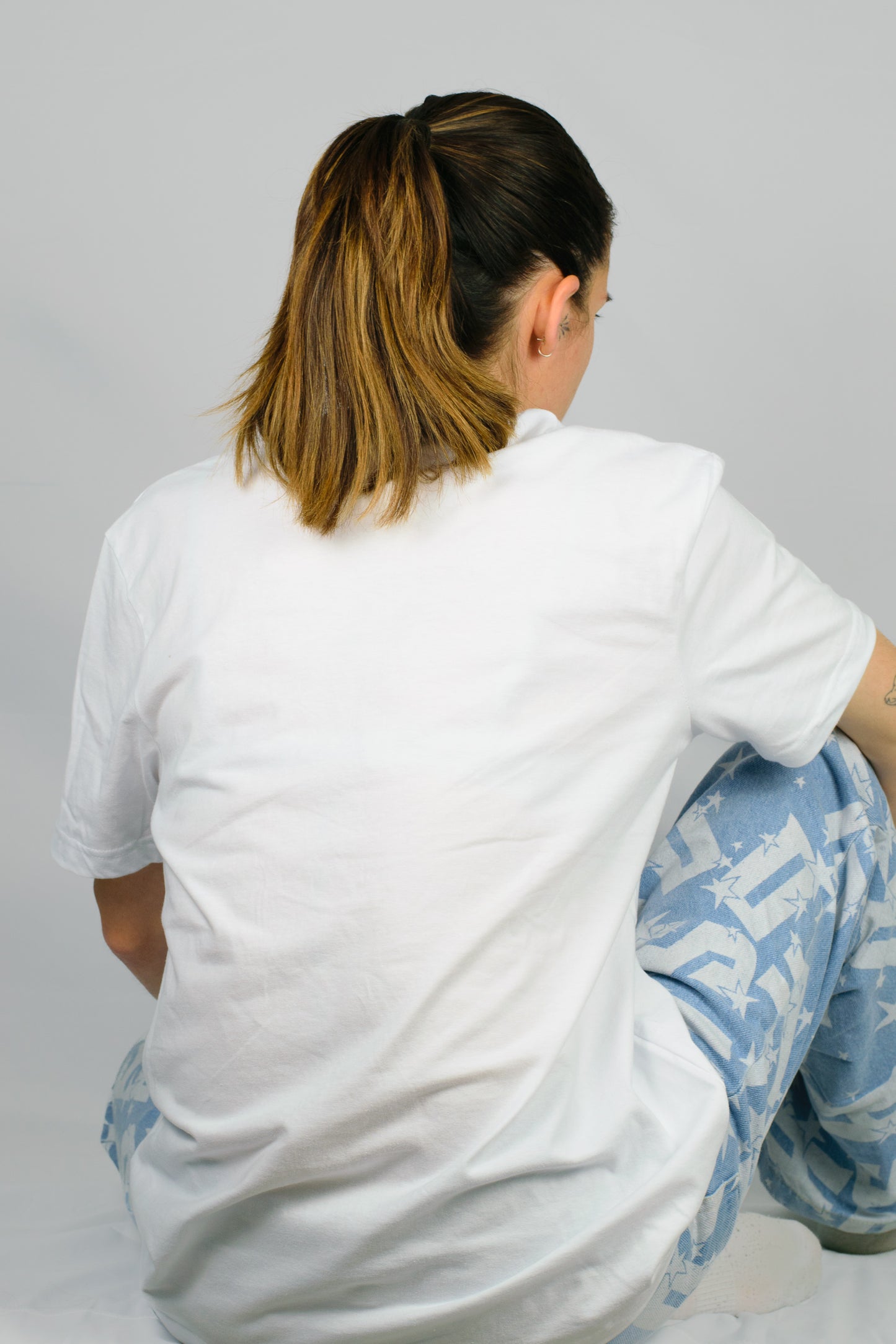 Person wearing a white Chances Clothing t-shirt and light blue pants with text sitting on a grey background