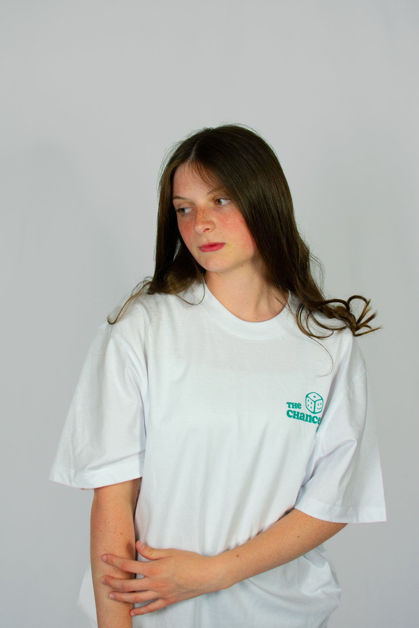 Person wearing a white t-shirt with a small green smiley dice logo on a grey background
