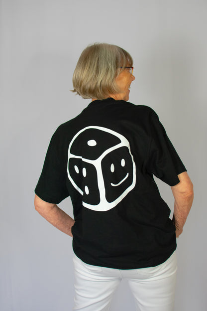 Person wearing a black Chances Clothing t-shirt with a white smiley dice design on the back against a grey background