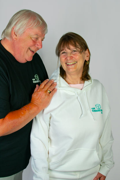 Two elderly people wearing a white hoodie and a black tee with a smiley dice logo stood in front of a grey background