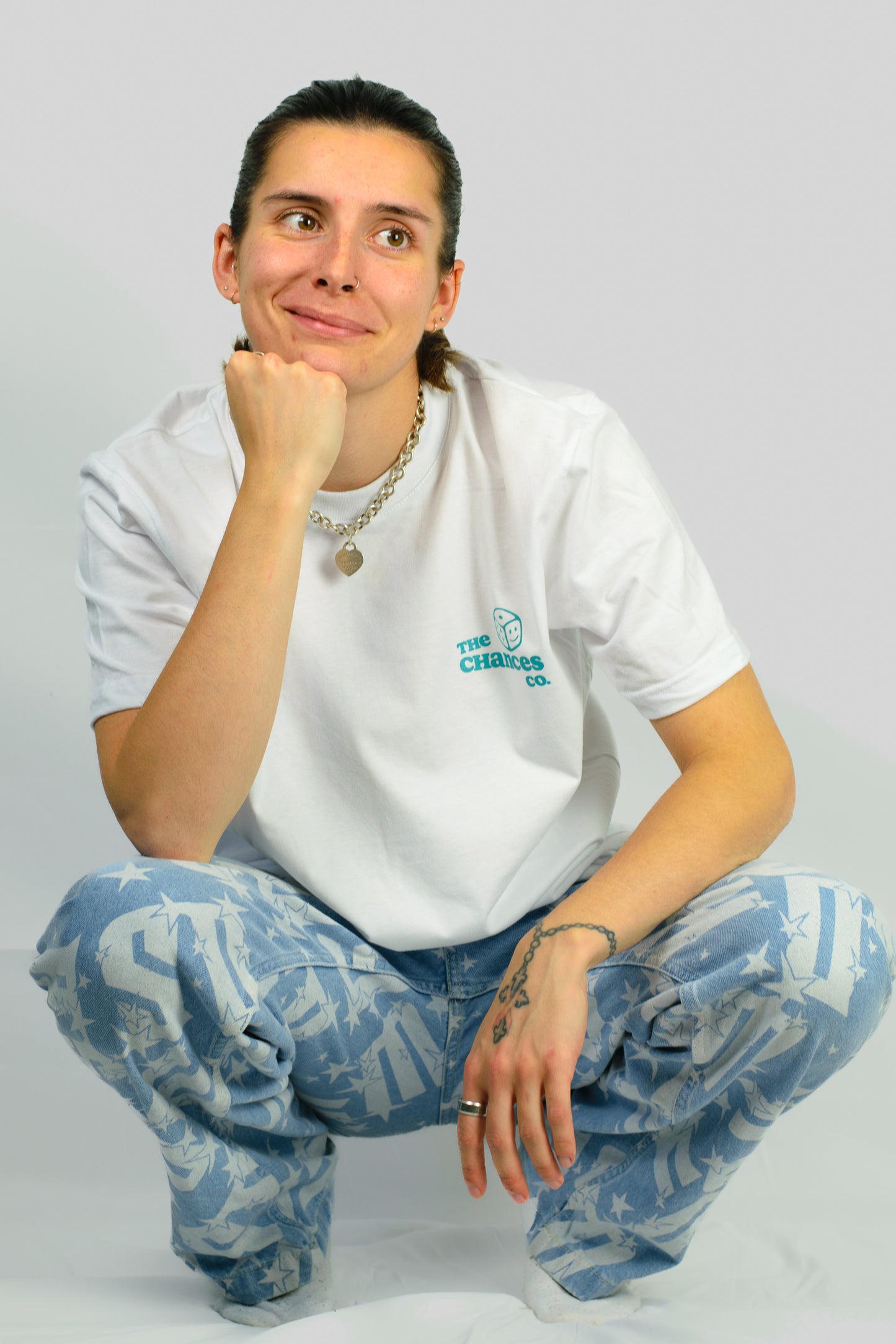 Person wearing a white t-shirt with a green smiley dice logo and the chances co written next to it. Knelt in front of a plain background