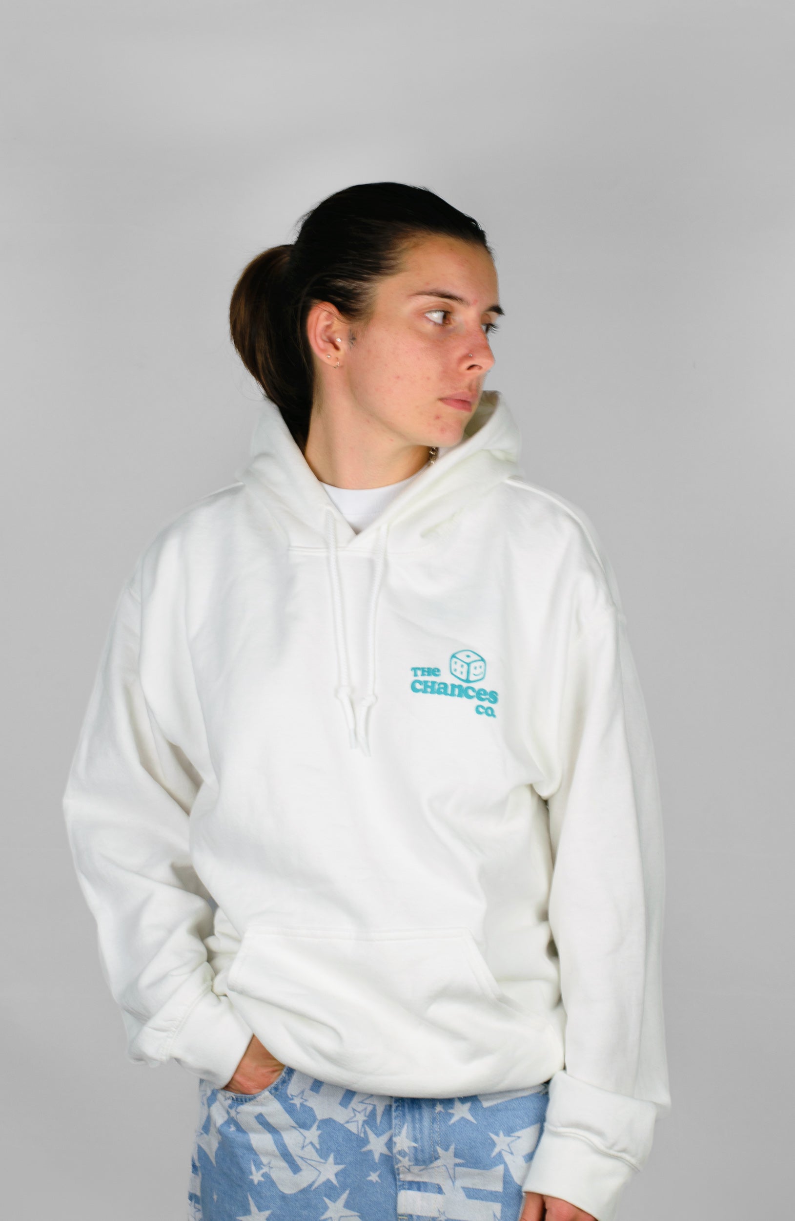 Person wearing a white hoodie with a green "the Chances Co" logo with a small smiley green dice. stood on a grey background