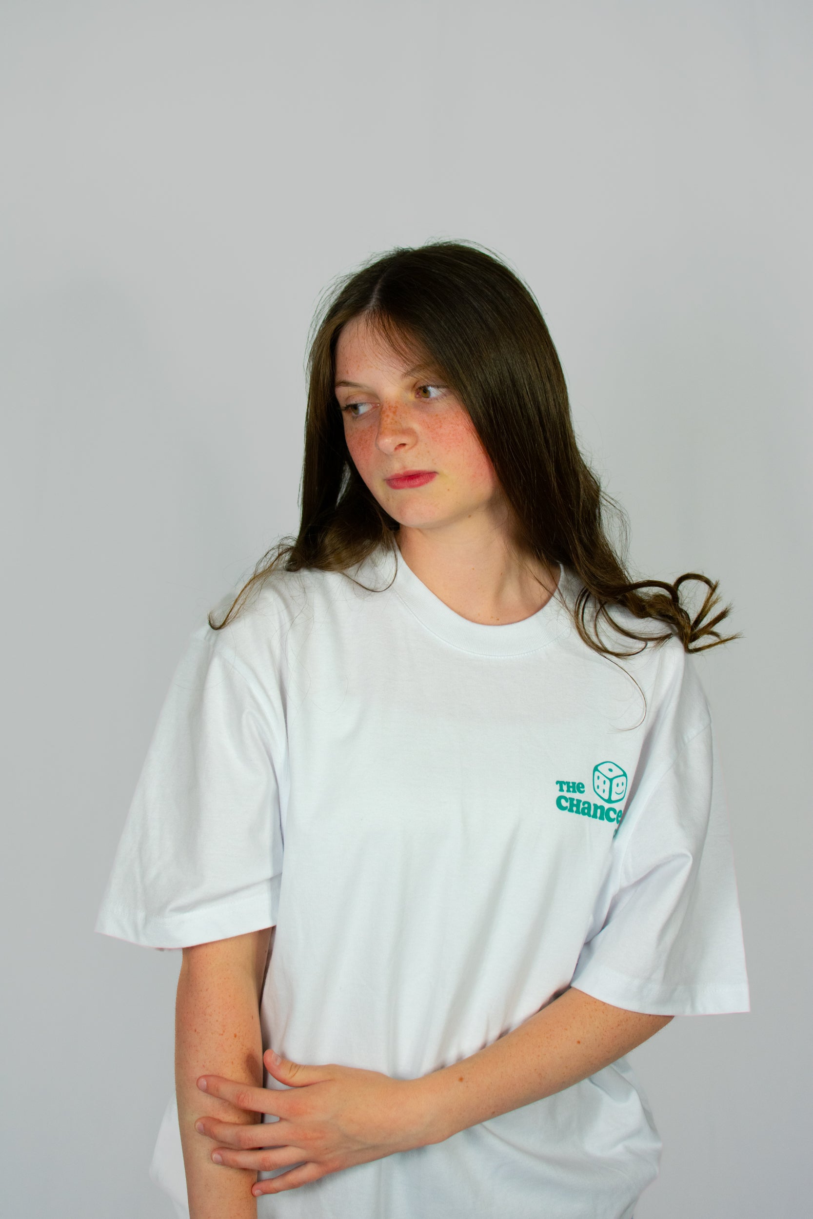 Person wearing a white t-shirt with a small green smiley dice logo on a grey background