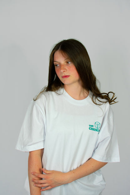 Person wearing a white t-shirt with a small green smiley dice logo on a grey background