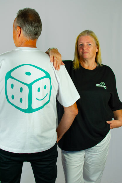 Two people, one wearing a white t-shirt with a green smiley dice design and the other in a black t-shirt with a small dice and the chances co logo, standing against a plain background.