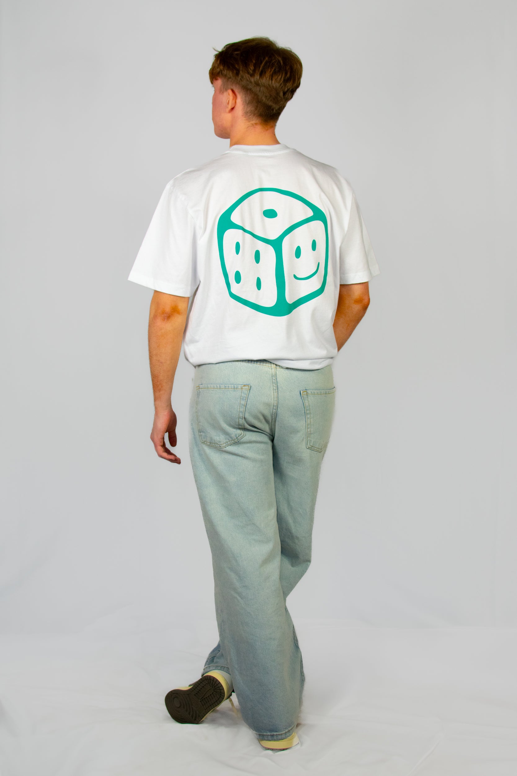 Person wearing a white t-shirt with a green smiley dice design on the back, standing against a plain background.