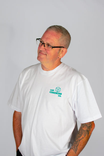 Man wearing a white t-shirt with a green smiley dice logo with "the Chances Co" written next to it stood in front of a plain background