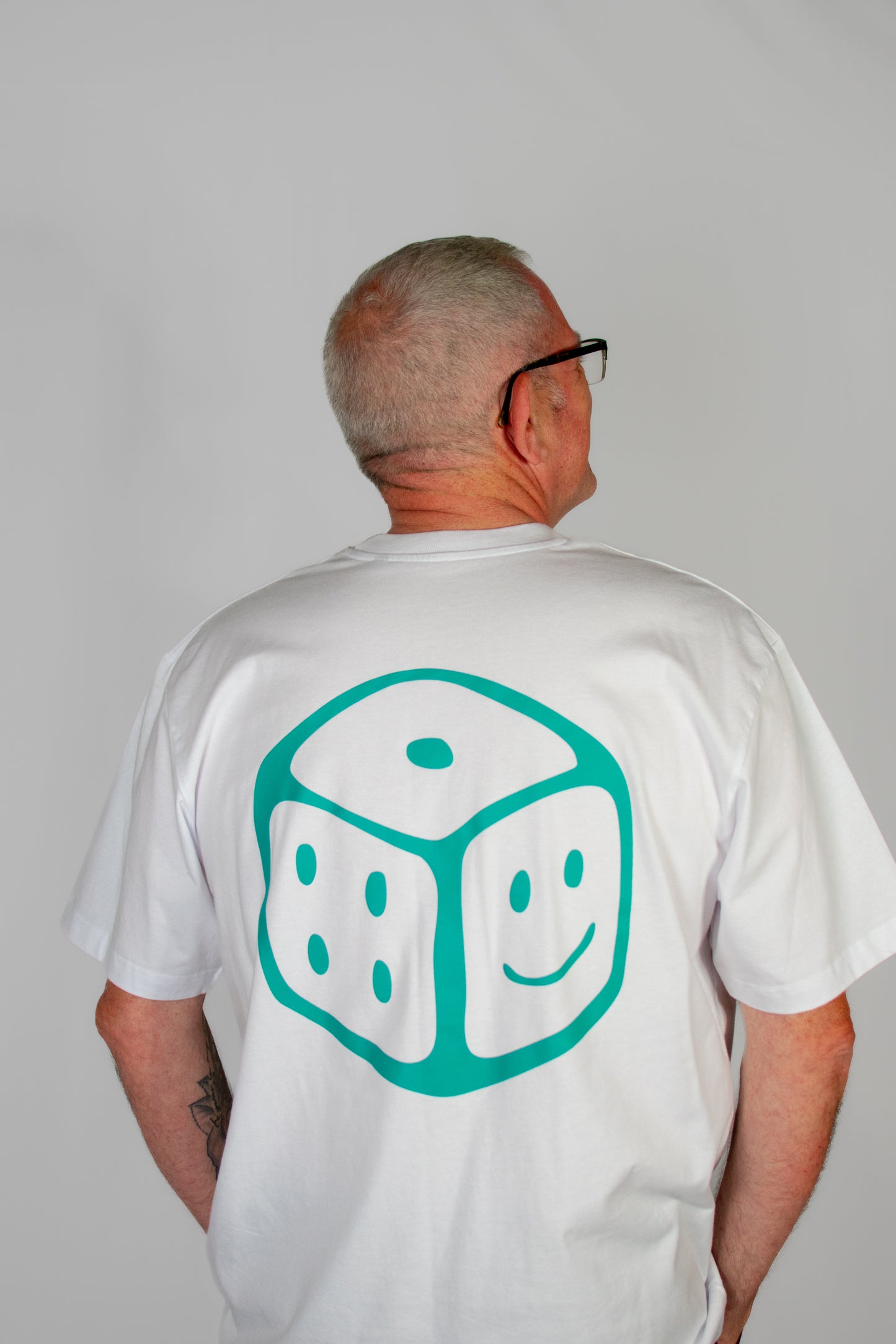Person wearing a white t-shirt with a green smiley dice design on the back against a grey background