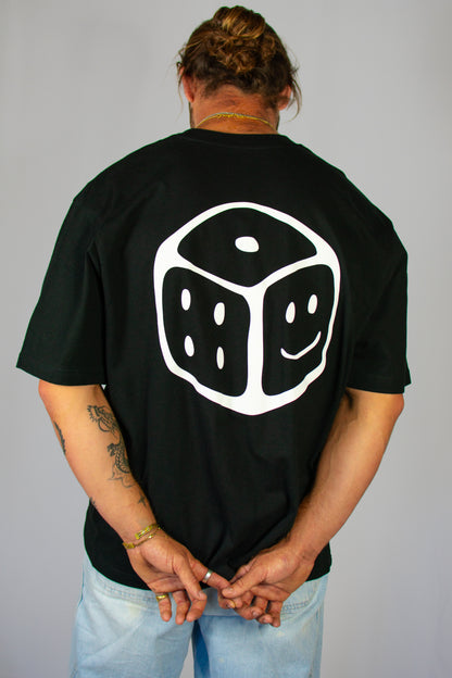 Person wearing a black t-shirt with a white smiley dice design on the back, standing against a plain background.