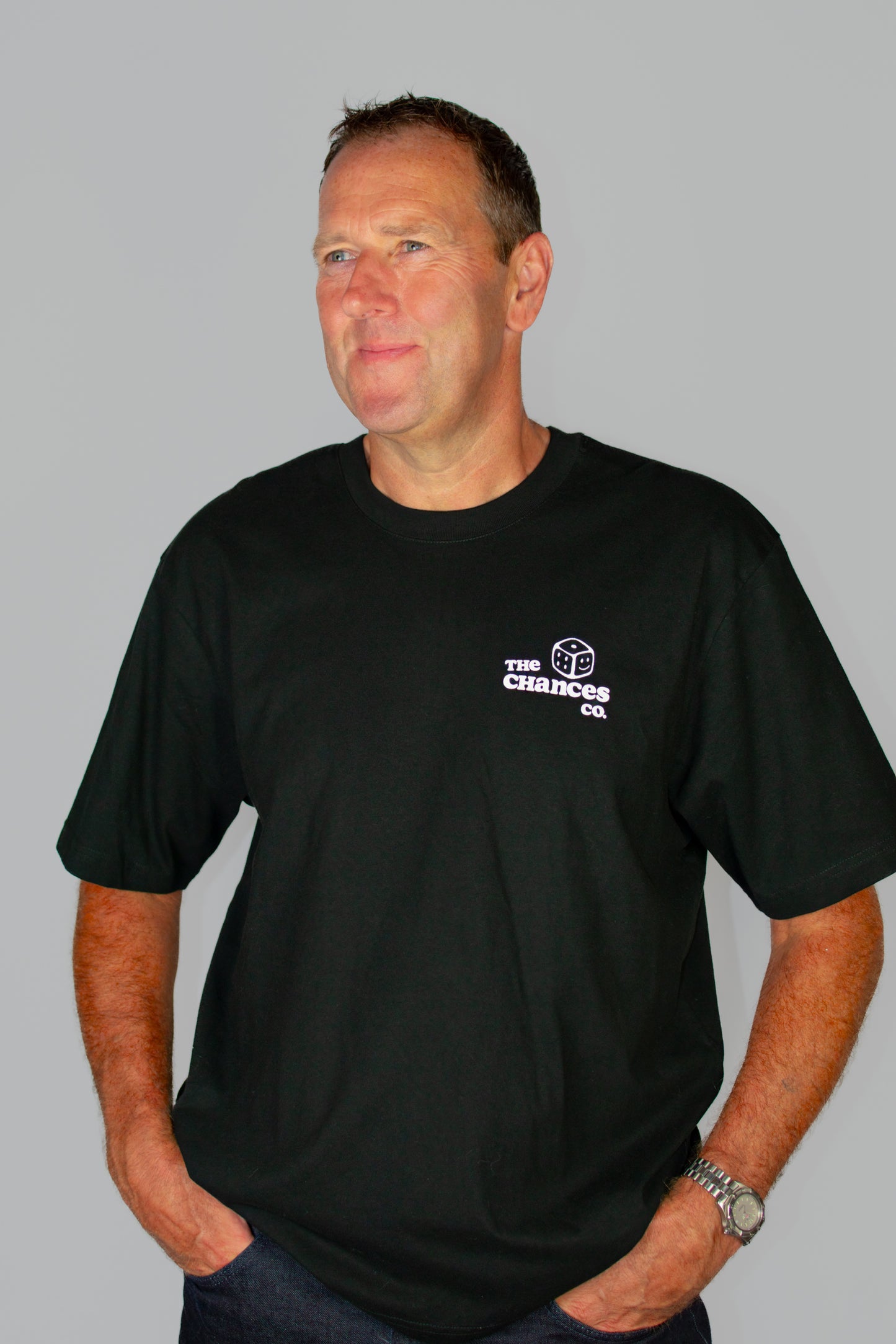 Man wearing a black t-shirt with a white dice logo and "the chances co" written next to it stood on a grey background