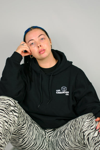 Person wearing a black Chances hoodie with a white smiley dice logo, sitting against a plain background