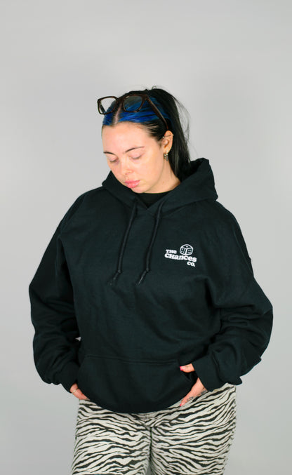 Person wearing a black hoodie with a small white dice logo on a grey background