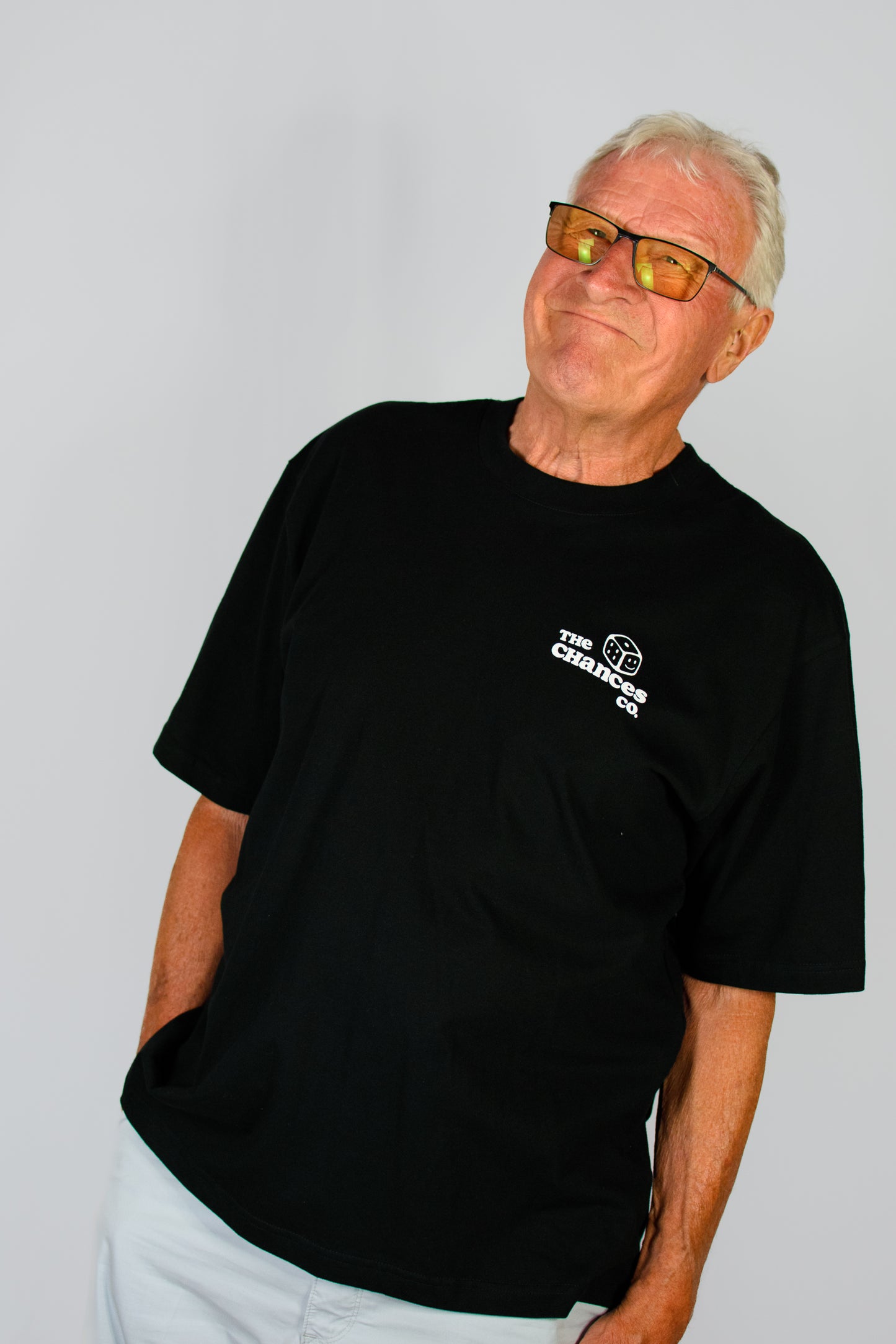 Man wearing a black t-shirt with a white dice logo and the chances co written on stood in front of a plain background