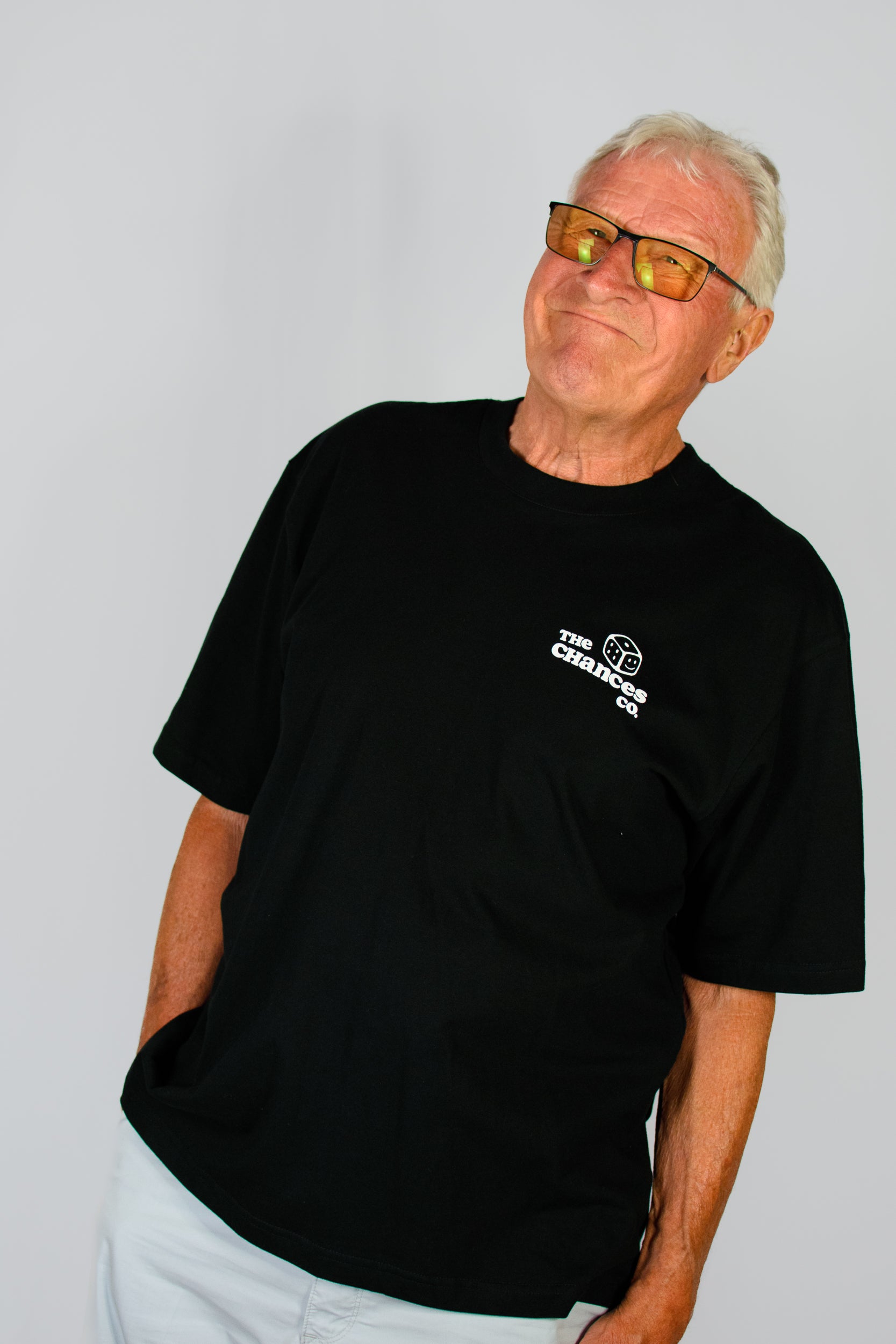 Man wearing a black t-shirt with a white dice logo and the chances co written on stood in front of a plain background