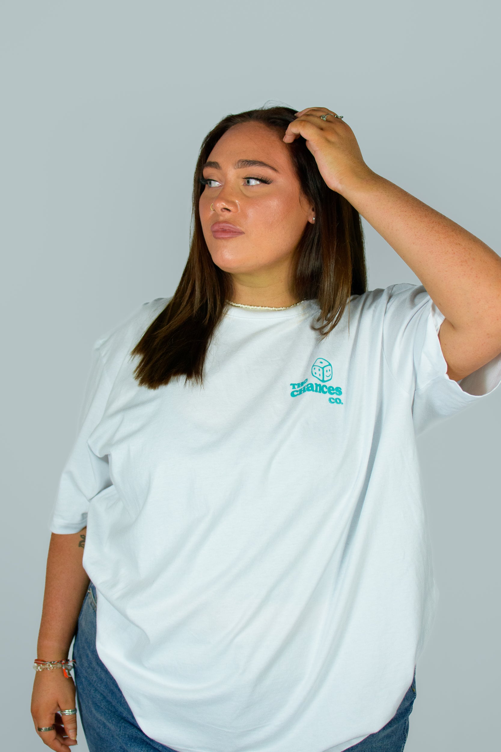 Girl wearing a white Chances Clothing T-shirt which has a Small smiley green dice on front and "the Chances Co" written next to it.